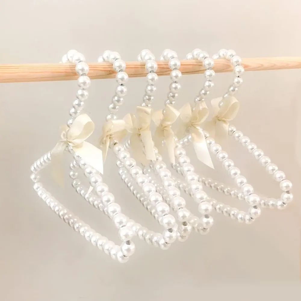 Small ivory pearl beaded kids hangers with satin bows on a wooden rail